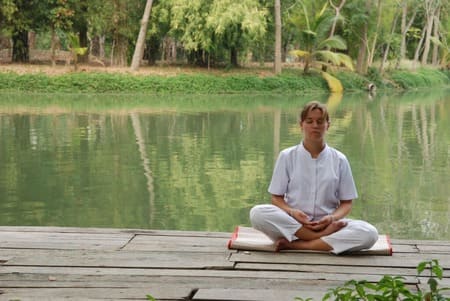 foto de uma mulher sentada meditando em um pier. Ela veste camisa e calça brancas. O pier está na beira de um lago. A foto ilustra deste arquivo do site Ori Mystyco.
