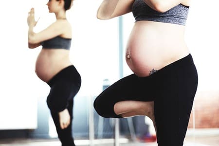 Foto de mulher grávia com top e calça preta fazendo yoga. A foto ilustra este artigo do site Ori Mystyco.
