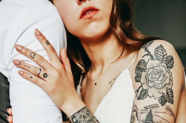 Imagem de uma mão de mulher segurando e prendendo o braço de um homem. A mulher tem tatuagens preto e branca com desenhos de rosa no braço. A foto ilustra o artigo Amor ou apego? O que você sente? do site Ori Mystyco.