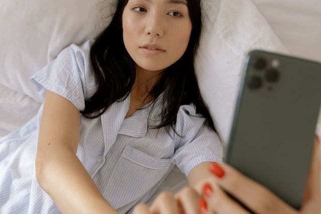 Foto de uma mulher japonesa deitada na cama tirando uma selfie assim que acorda. A foto ilustra o artigo O Ego destrói sua Felicidade do site Ori Mystyco.
