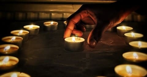 Foto de uma pessoa colocando uma vela pequena no centro de um círculo feito com as mesmas velas. As velas estão sobre uma mesa. A foto é usada para ilustrar o artigo Magia das Velas. Como praticá-la e quando? do site Ori Mystyco.