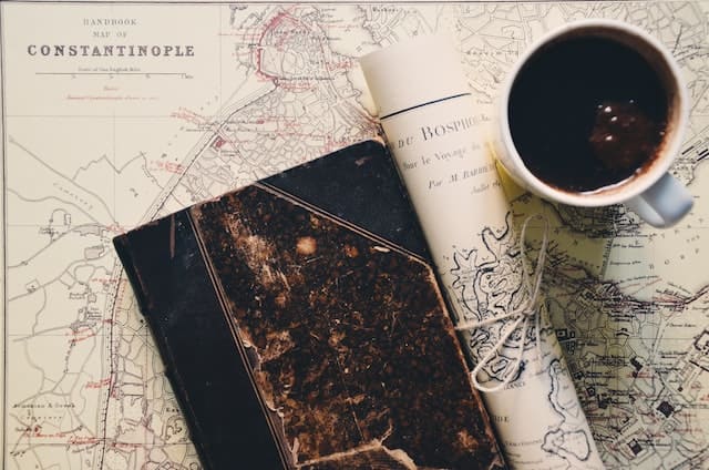 Foto de um mapa, e em cima dele uma agenda com os astros do céu e uma xícara de café. A imagem serve para ilustrar o artigo O que é um Stellium na astrologia? Saiba aqui! do site Ori Mystyco.