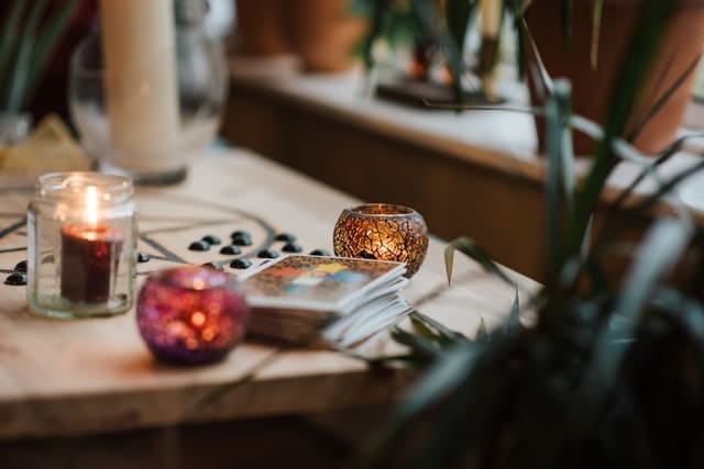 Imagem de Baralho Cigano sobre uma mesa de madeiras com velas acessas em pequenos rechauds. Esta foto serve para ilustrar a tirada de Baralho Cigano online - Leitura Grátis de 3 cartas do site Ori Mystyco.