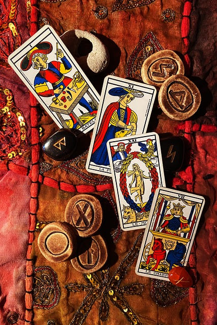 Foto de cartas do Tarot de Marselha sobre uma mesa esotérica com runas de pedra e runas de madeira para ilustrar a página que contém a tirada de Tarot de Marselha Online Grátis do Site Ori Mystyco.