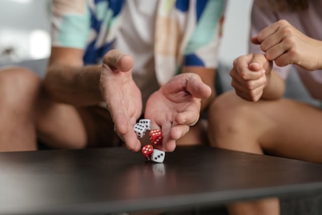 Foto de mãos jogando dados sobre uma mesa. Ao lado, pode-se ver a mão de uma segunda pessoa. Foto utilizada para ilustrar a Dominomancia online Leitura de Dominós Online Ori Mystyco