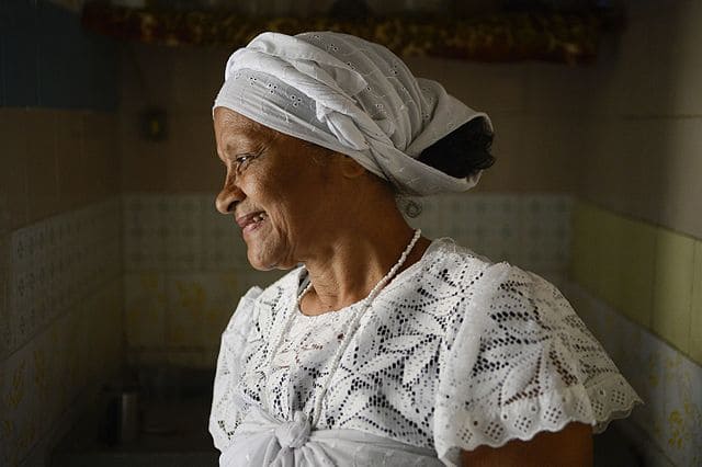 Foto de uma mulher preta com roupa e lenço de renda branca. A foto ilustra o artigo O que é Candomblé do site Ori Mystyco.