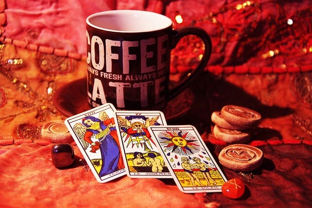 Imagem de algumas cartas de tarot de Marselha sobre uma mesa com umacabeca preta com a palavra Coffe Latte escrito em branco e runas de pedra e madeira. A imagem é usada para a Tirada de tarot Financeiro Grátis Online, ou Tarot do Dinheiro Grátis Online do site Ori Mystyco.